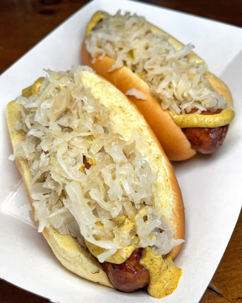 Two bratwurst sausage with sauerkraut and mustard on a paper plate.