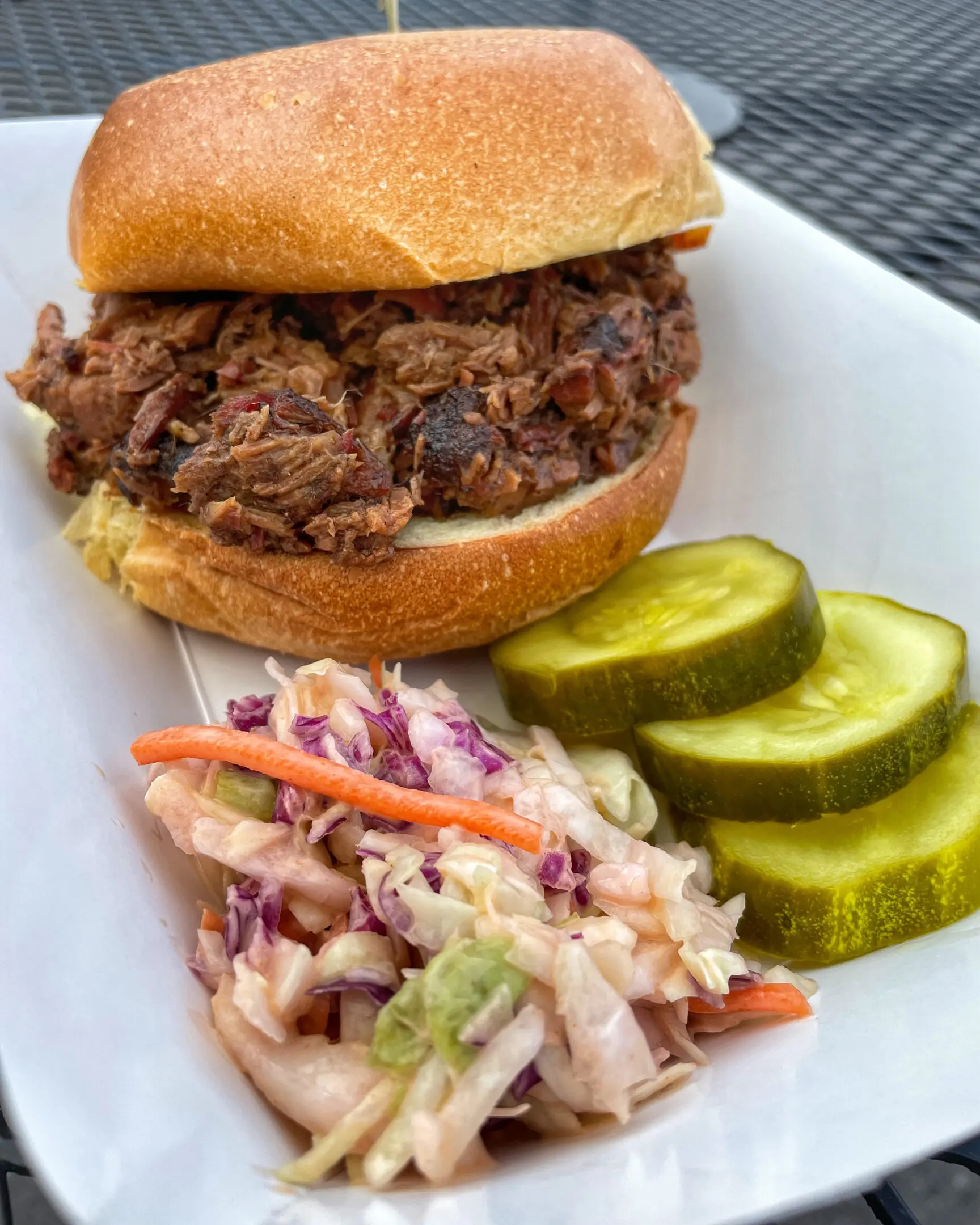 A plate with a sandwich, coleslaw and pickles.