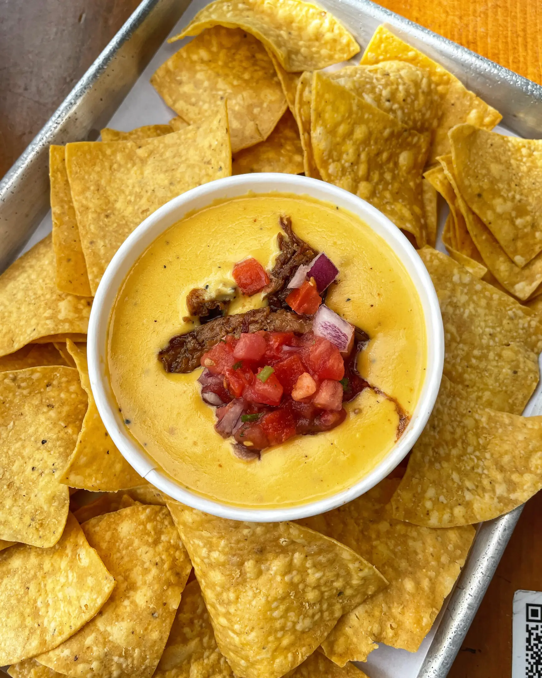 A bowl of cheese dip surrounded by tortilla chips.